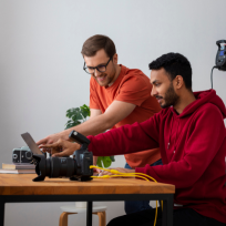 Two men using a laptop together in an office environment discussing post-production video making.